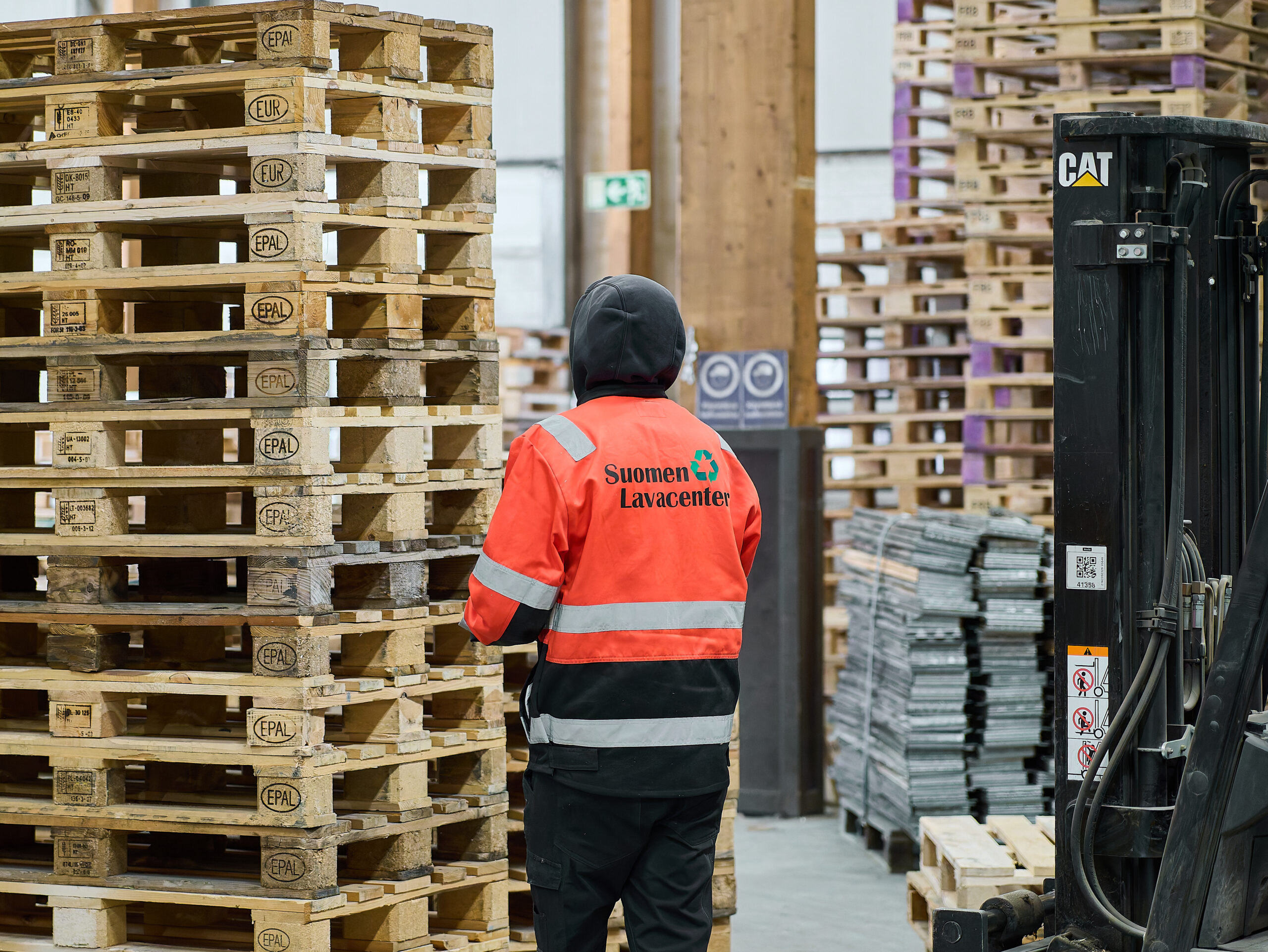 Suomen Lavacenterin työntekijä tarkastamassa pinottuja käytettyjä kuormalavoja trukin vieressä varastolla